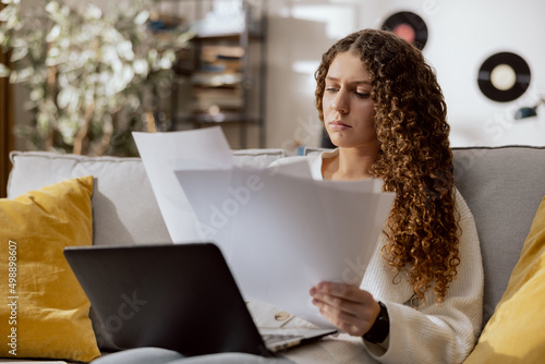 Εκτύπωση καμβά A woman with curly hair sits on the couch in the living room in the afternoon with a laptop on lap