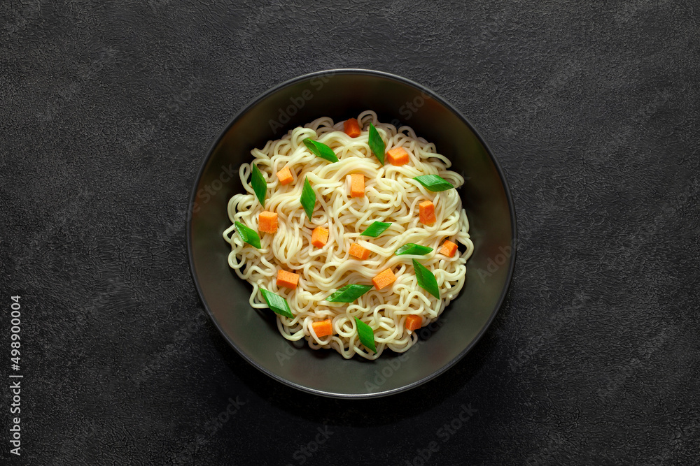 Instant noodles with vegetables in bowl, on dark background, top view, space to copy text.