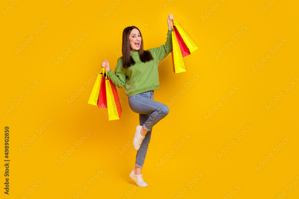Full length body size view of attractive cheerful woman holding bags dancing isolated over bright yellow color background Full length body size view of attractive cheerful woman holding bags dancing isolated over bright yellow color background