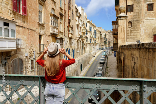 Tourist woman holds hat on iron bridge looking the old town of Valletta, Malta