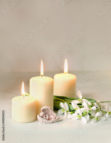 Cute sleeping angel  snowdrops flowers and candles on table  blurred  abstract background. Religious church holiday. symbol of faith in God  Christianity Feast. Romantic relaxation composition
