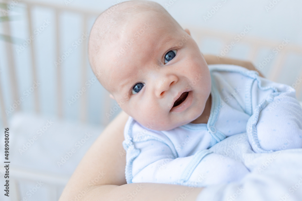 a newborn baby boy in his mother's arms near the crib at home, parental love and care for the baby in the first days after birth a newborn baby boy in his mother's arms near the crib at home, parental love and care for the baby in the first days after birth