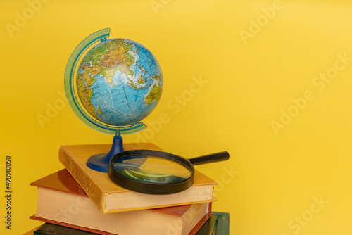 Stacks of books, globe and magnifying glass on the yellow background with copy space for text. World Book Day. Education background. Literacy day. Back to school