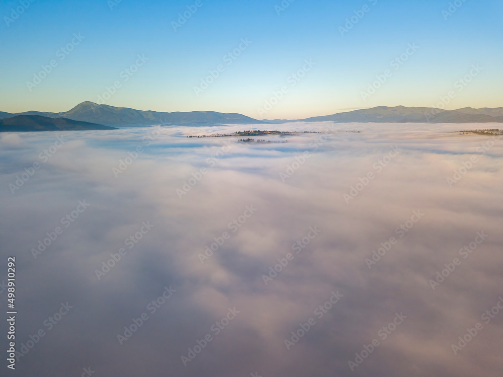 Flight over fog in Ukrainian Carpathians in summer. Mountains on the horizon. A thick layer of fog covers the mountains with a continuous carpet. Aerial drone view.