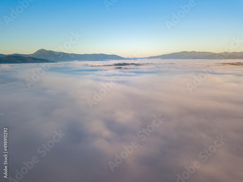 Flight over fog in Ukrainian Carpathians in summer. Mountains on the horizon. A thick layer of fog covers the mountains with a continuous carpet. Aerial drone view. © Sergey