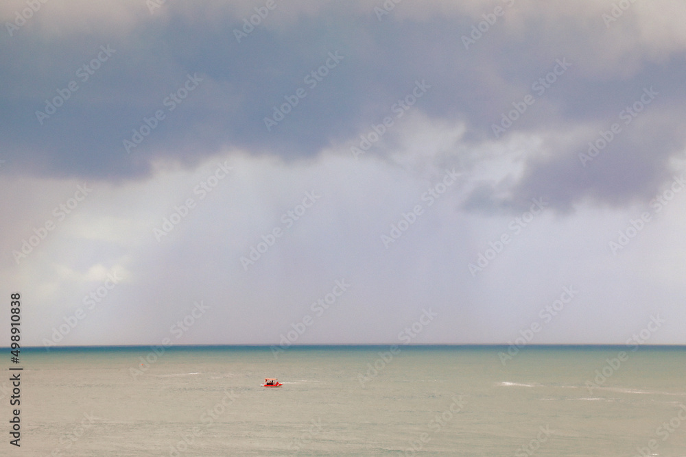 Small red fishing boat on the bay under heavy dark storm clouds at Forster, NSW Australia