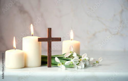 Wooden cross  snowdrops flowers and candles on table  blurred abstract background. Religious church holiday. symbol of faith in God  Christianity Feast  Easter  Palm Sunday  Lent