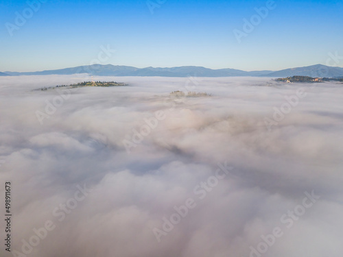 Flight over fog in Ukrainian Carpathians in summer. Mountains on the horizon. A thick layer of fog covers the mountains with a continuous carpet. Aerial drone view.