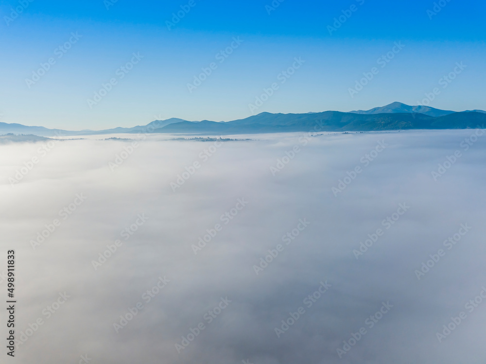 Flight over fog in Ukrainian Carpathians in summer. Mountains on the horizon. A thick layer of fog covers the mountains with a continuous carpet. Aerial drone view. Flight over fog in Ukrainian Carpathians in summer. Mountains on the horizon. A thick layer of fog covers the mountains with a continuous carpet. Aerial drone view.