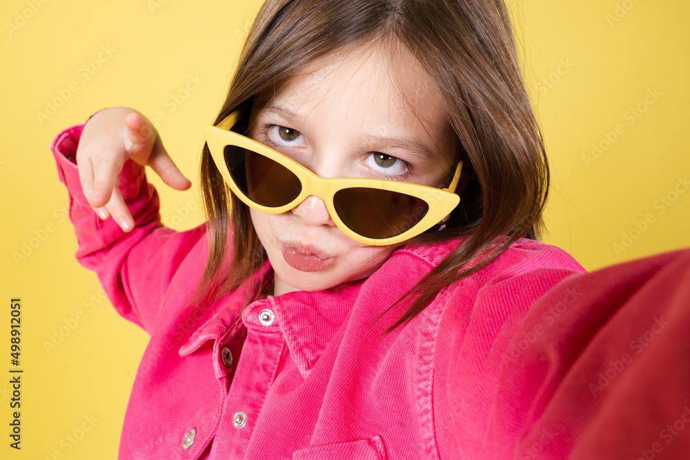 Arrogant little girl wearing sunglasses taking a selfie isolated on yellow background. Arrogant little girl wearing sunglasses taking a selfie isolated on yellow background.