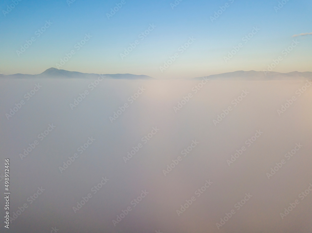 Fototapeta premium Flight over fog in Ukrainian Carpathians in summer. Mountains on the horizon. A thick layer of fog covers the mountains with a continuous carpet. Aerial drone view.