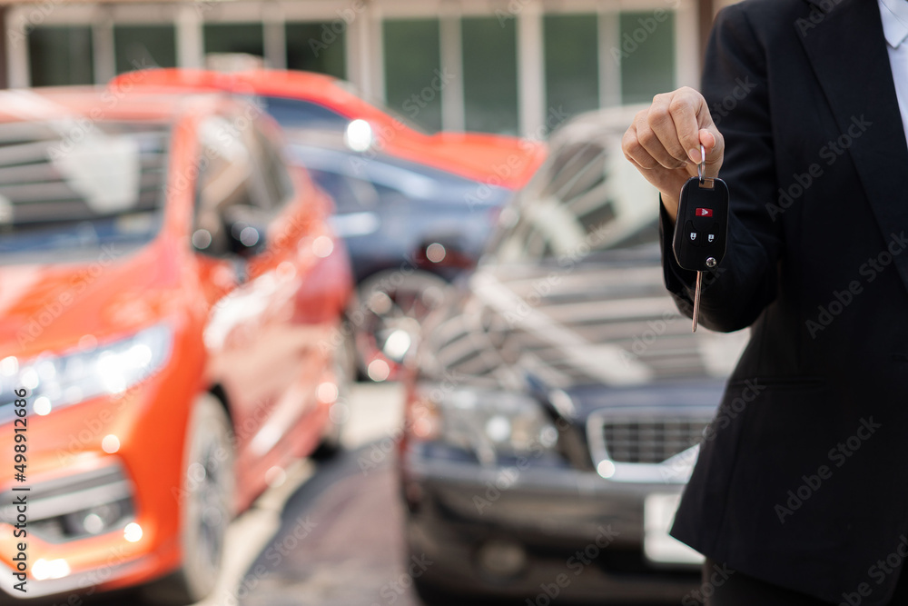 Obraz premium Businessman holding car keys in front and new car behind Parking in front of the house Offered to customers at showrooms with low-interest offers. Special promotion, transportation concept.