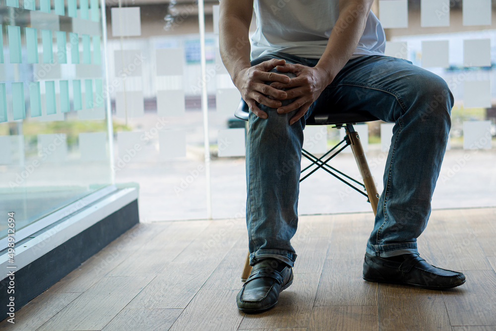 The man sat on his chair, clutching his knees in pain. suffering from osteoarthritis medical concept The man sat on his chair, clutching his knees in pain. suffering from osteoarthritis medical concept
