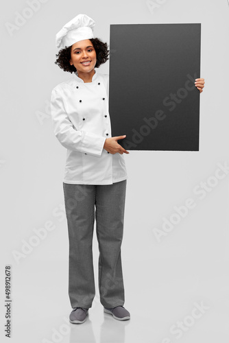 cooking, advertisement and people concept - happy smiling female chef in toque holding black chalkboard over grey background