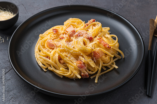 Pasta carbonara with bacon, cheese and egg on a dark background.