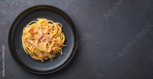 Linguini pasta with carbonara sauce on a dark background. Carbonara sauce made of bacon, parmesan, eggs, cream and pepper.