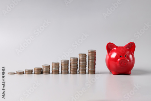 Billede på lærred Stack of coins in ascending order and red piggy bank on table, profitable invest