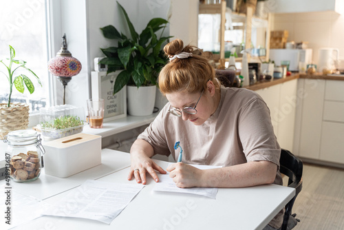 Caucasian Woman in beige t-shirt sign documents at home. Remote work. Sign model release. Filling out documents, positive paperwork