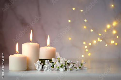 Cute angels  snowdrops flowers and candles on table  blurred abstract background. Religious church holiday. symbol of faith in God  Christianity Feast. Romantic relaxation composition