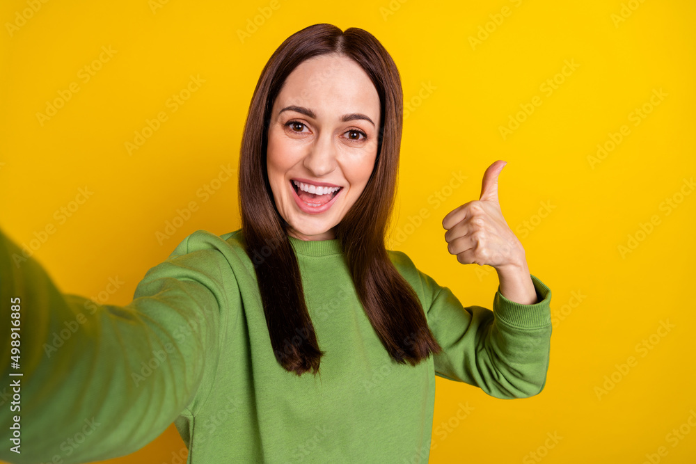 Self-portrait of attractive cheerful woman showing thumbup isolated over bright yellow color background Self-portrait of attractive cheerful woman showing thumbup isolated over bright yellow color background