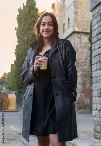 Three quarter length photo of a gorgeous latina young woman holding a coffee cup while is standing in a square of Barcelona center and is looking at the camera