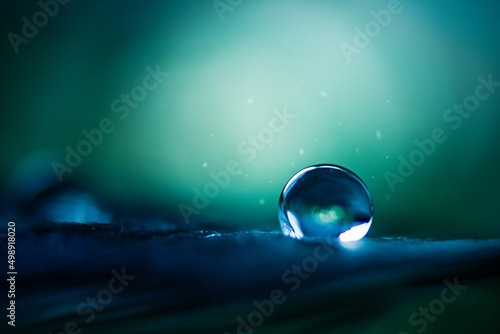 A drop of water in dark green and blue tones in the light. © Yuliya