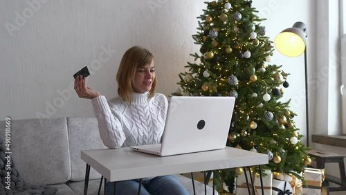 Cute girl is having converstation on the internet, video call, woman is showing her credit card to the caller. Buying Christmas presents and gifts online, online communication concept.  photo