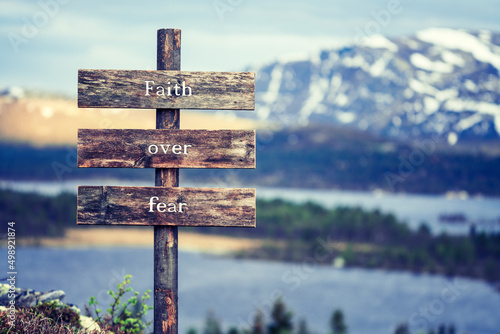 faith over fear text quote written on wooden signpost outdoors in nature with lake and mountain scenery in the background. Moody feeling. photo