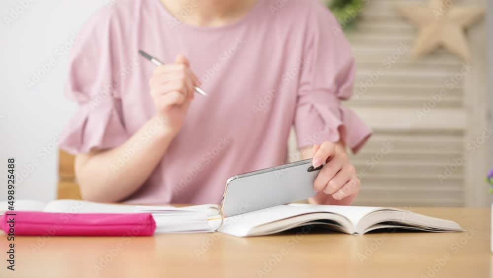 スマートフォンを観ながら勉強をする女性 スマートフォンを観ながら勉強をする女性