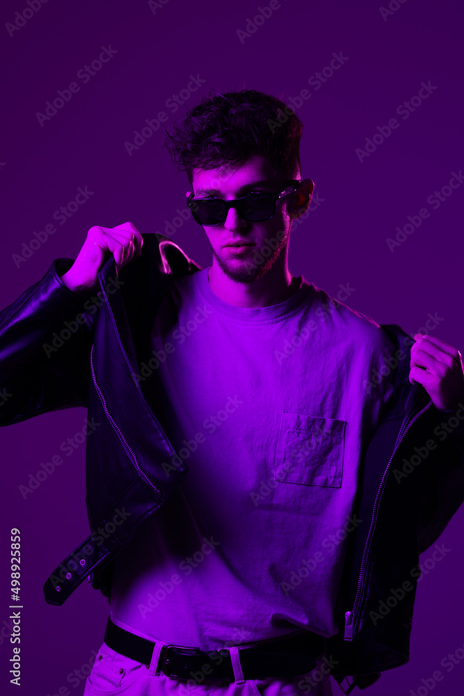 Young man's portrait isolated on blue studio background in neon light. Beautiful male model in leather wear. Concept of human emotions, facial expression, sales, ad. Young man's portrait isolated on blue studio background in neon light. Beautiful male model in leather wear. Concept of human emotions, facial expression, sales, ad.