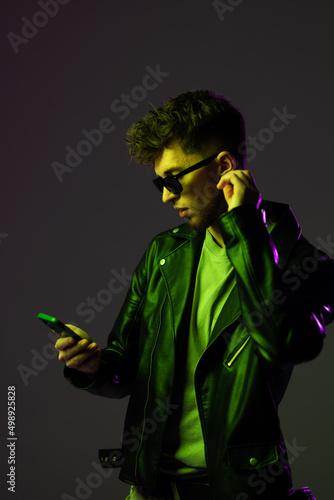 Portrait of man in glasses attentively looking at phone, reeading message isolated over blue background in neon lights. Concept of human emotions, facial expression, lifestyle. Copy space for ad photo