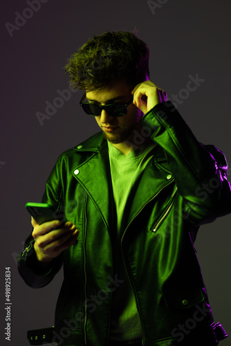 Portrait of man in glasses attentively looking at phone, reeading message isolated over blue background in neon lights. Concept of human emotions, facial expression, lifestyle. Copy space for ad photo