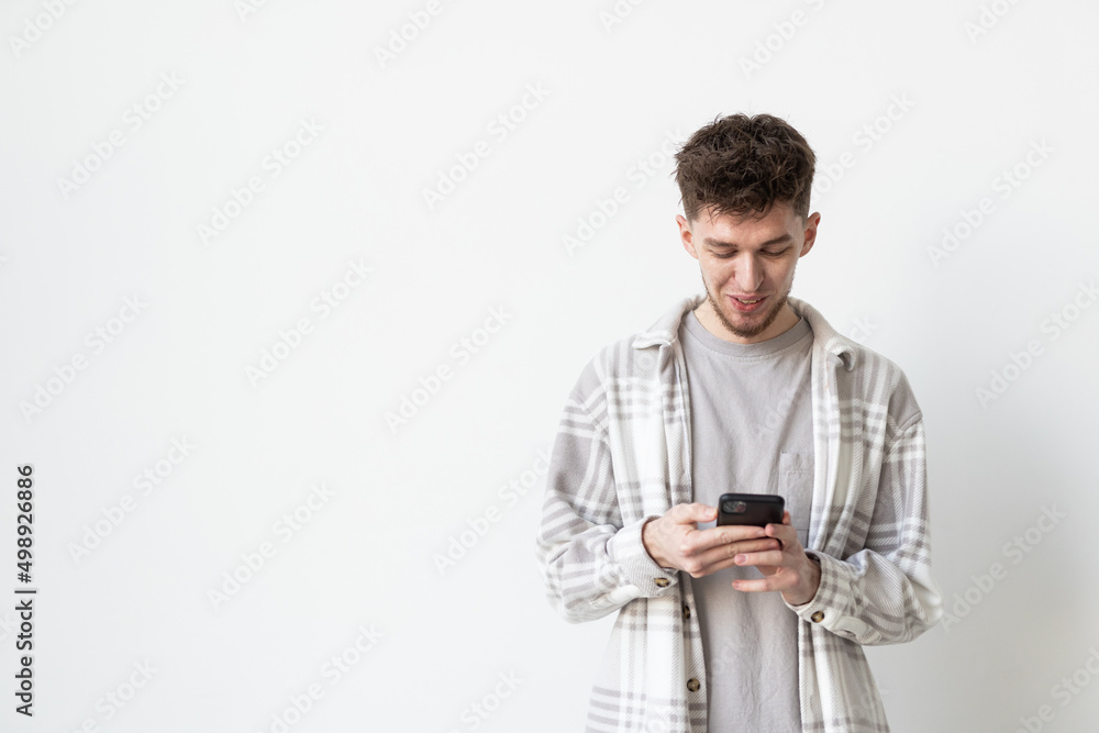 Good news from friend. Confident young handsome man in jeans shirt holding smart phone and looking at it with smile while standing against white background Good news from friend. Confident young handsome man in jeans shirt holding smart phone and looking at it with smile while standing against white background