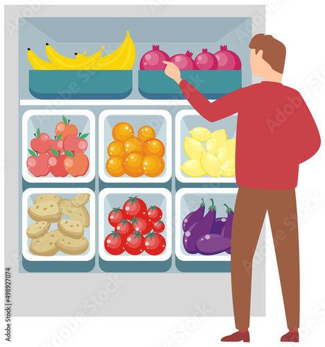 Young man doing grocery shopping at supermarket, takes products from shelf in daily life choosing fruits and vegetables. Consumer making choice of healthy organic food in market buying in greengrocery