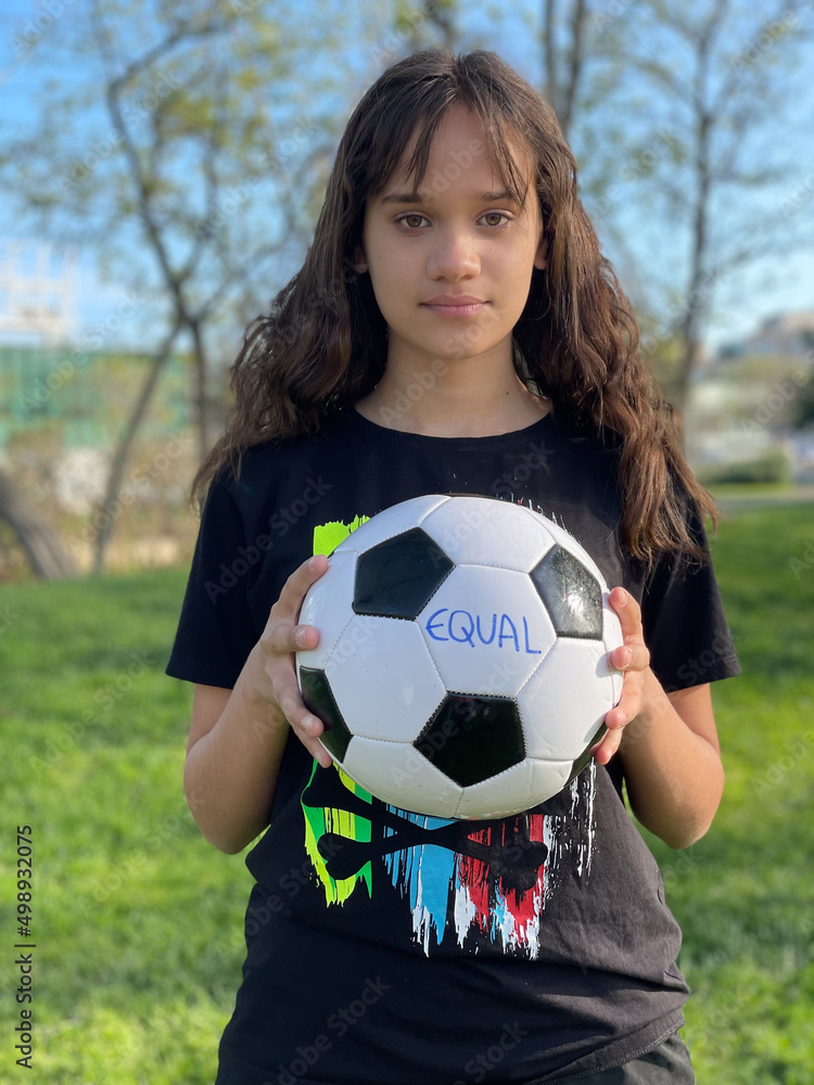 Beautiful teenager holds a soccer ball showing the word equality. Active youth concept