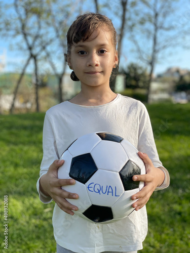 Beautiful girl holds a soccer ball showing the word equality. Active childhood concept © dianix!