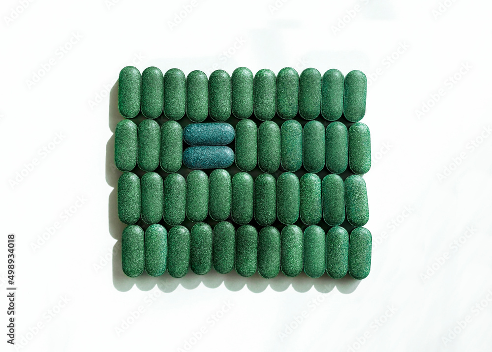 Chlorella, spirulina or barley grass in pill shaped rows and two blue pills across on white background Nutritional supplement, detox superfood health care Chlorella, spirulina or barley grass in pill shaped rows and two blue pills across on white background Nutritional supplement, detox superfood health care