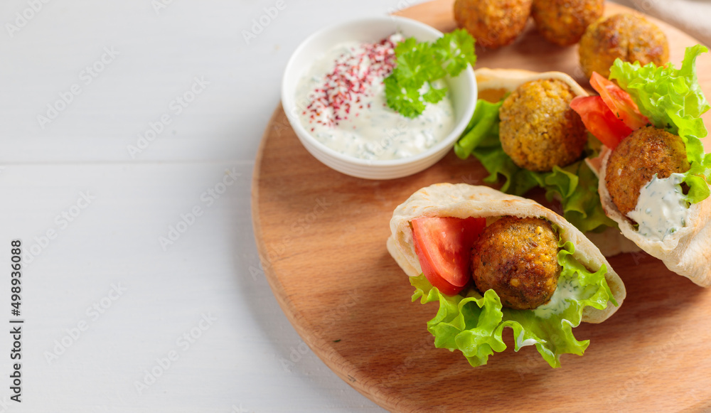 Two mini pitas with falafel, sauce and fresh vegetables. On a round wooden tray. Close-up, copy of the space