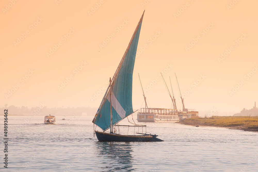 felucca is a traditional sailing boat used for tourist transport and cruise down the Nile in Luxor city in Egypt at romantic sunset time