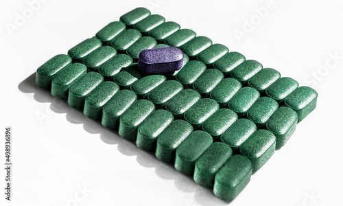Fotografia Pills of chlorella, spirulina, barley grass close-up lined up in rows on white b