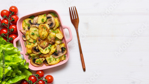 Bacon tartiflette on a baking dish with herbs and vegetables at home on a wooden white background. View from above. The national dish of potatoes. copy space