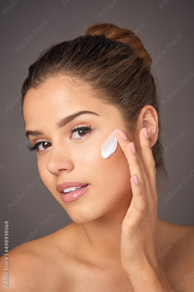 Your skin is worth investing in. Portrait of a youthful model applying moisturizer to her face in studio.