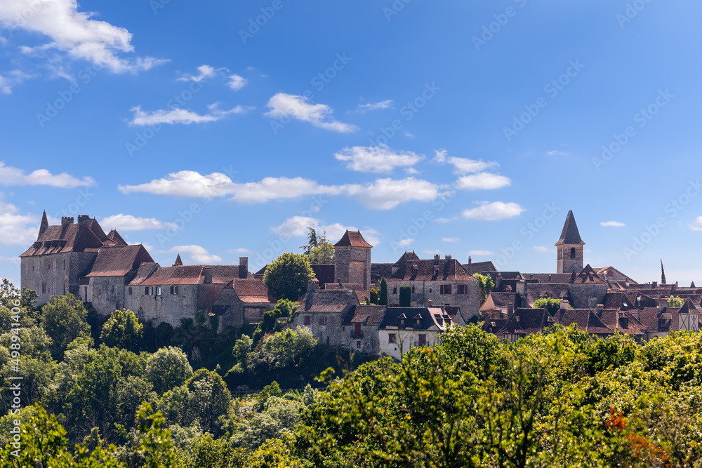 Panoramic view of ancient Loubressac village on sunny summer day against blue sky and forest in foreground. Lot, Occitania, Southwestern France