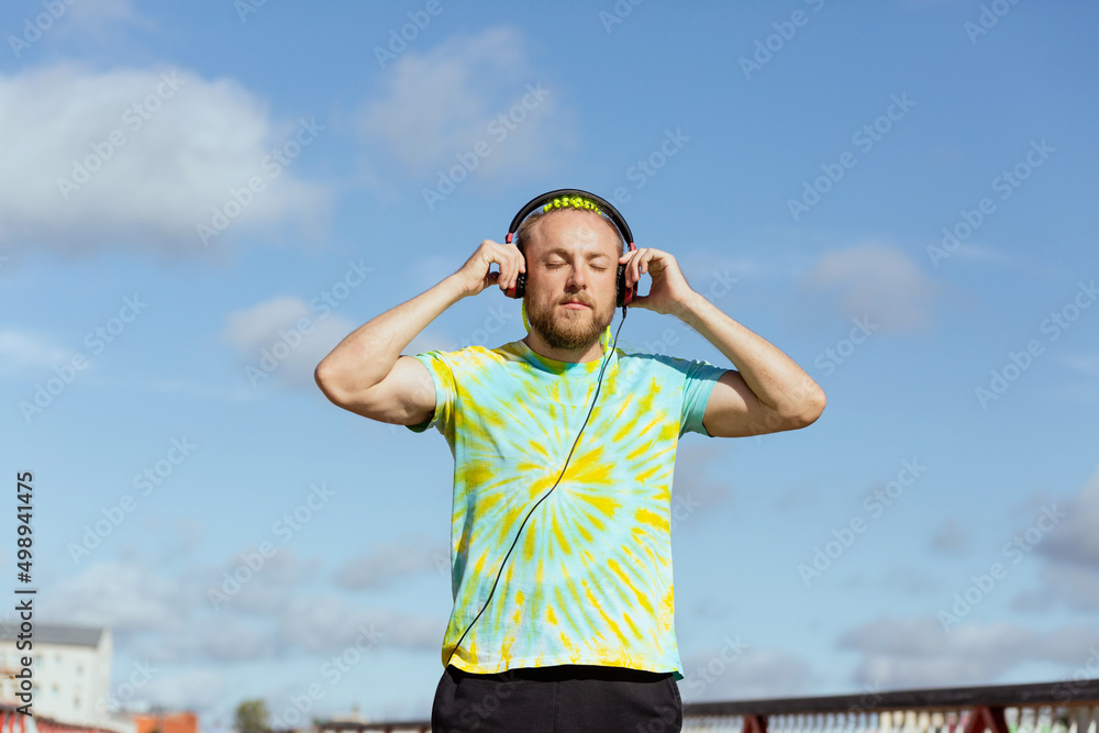 A man with an interesting mohawk hairstyle stands on the bridge wearing headphones around his neck