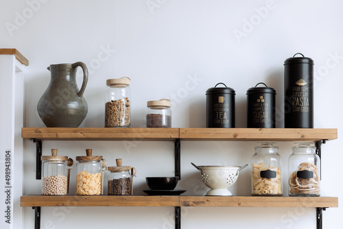 a jar of pasta, dishes for bulk products on a wooden shelf, in the kitchen. Shelves in the kitchen. System and organization of storage of bulk products in the kitchen. A jar for sugar, grain, cereals.