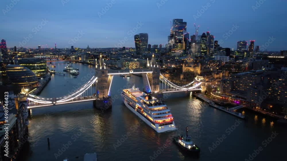 Aerial view of the illuminated skyline of London with Tower Bridge lift and a cruise ship passing by on the Thames river during dusk Aerial view of the illuminated skyline of London with Tower Bridge lift and a cruise ship passing by on the Thames river during dusk