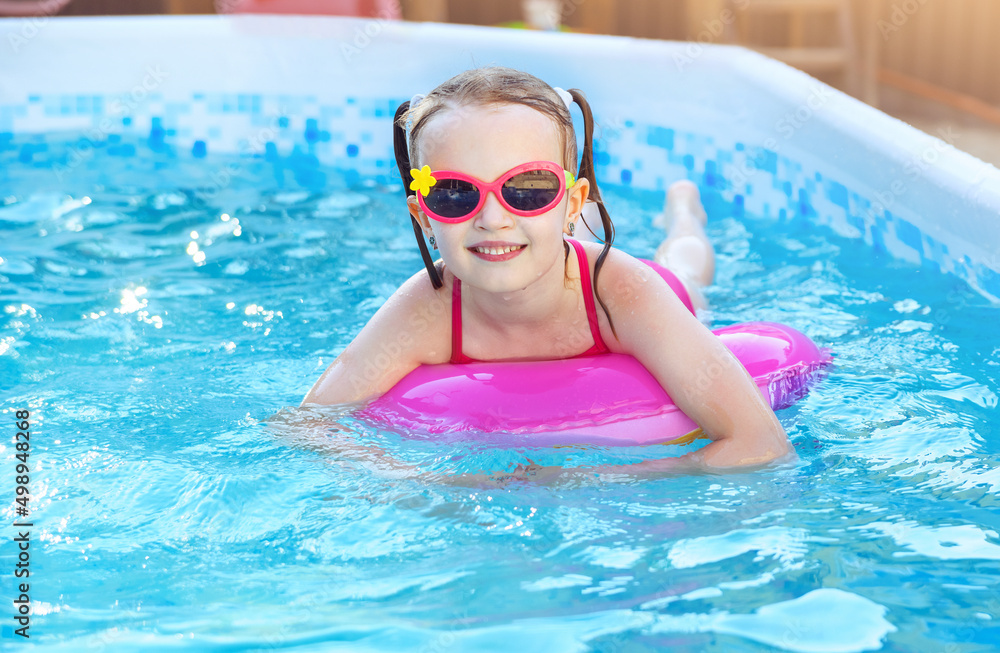 Child girl is splashing in frame swimming pool outdoor at home garden