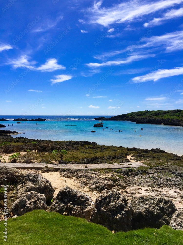 宮古島の真っ青なシギラビーチと青空と岩場の壮大な景色、そして遠くのボートパラソルと海水浴客