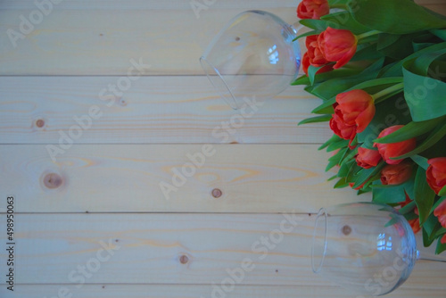 Pink tulips with green leaves lie in the upper corner on a wooden background, and wine glasses lie on the sides of the bouquet. High quality photo