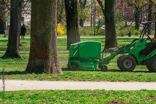 The municipal car cleans the green lawn of the city park in Krakow from old leaves and branches on a sunny day in April, side view